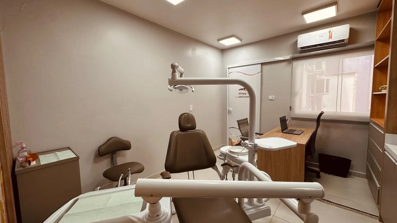 Consultório com cadeira odontológica caramelo, mesa de atendimento e janela